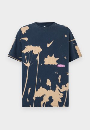 T-shirt Nike bleu marine à manches courtes avec des motifs floraux tie-dye beige et un petit logo Nike rose en bas à droite sur le devant.