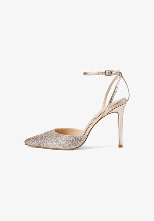 Zapato de tacón alto con punta puntiaguda, glitter dorado, correa en el tobillo y tacón de aguja, aislado sobre fondo blanco.