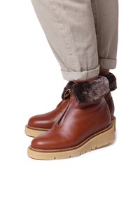 Botas de tobillo de cuero marrón con un puño de pelo sintético texturizado, que cuentan con un zipper frontal y una suela de plataforma beige sólida.