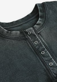 Sort henley-skjorte med struktureret stof, rund hals og fem knapper langs placket. Syet med sort tråd med uden søm finish.