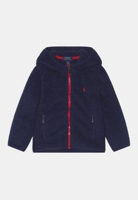 Marinblå fleecejacka med huva, röd dragkedja och sidfickor. Har en mjuk struktur och en liten logotypdetalj på bröstet.