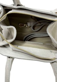 Světlé šedé semišové kabelka se zlatým zipem, obsahující jedno hlavní oddělení, odnímatelný popruh a několik vnitřních kapes a přepážek.