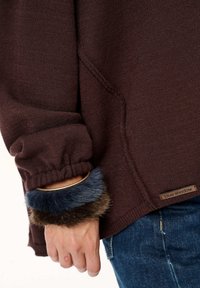 Ciemnoczerwony dzianinowy sweter o fakturowanym wzorze, z elastycznymi mankietami ozdobionymi sztucznym futrem w odcieniach niebieskiego i brązowego oraz naszywką z szyciem.