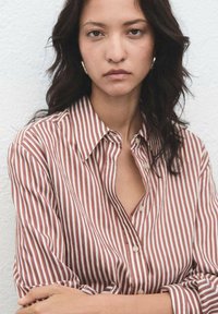 Striped button-up shirt with vertical red and white stripes, collar, and a relaxed fit. Fabric appears soft with a smooth texture.