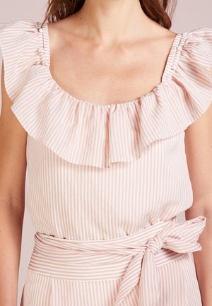 Kvinde iført en lyserød og hvid kjole med lodrette striber, flæsekant ved halsudskæringen, knapdetaljer på stropperne og et bundet bælte i taljen.