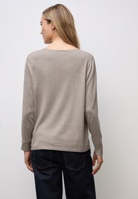 Beżowy sweter z długim rękawem, miękka tekstura, dekolt z tyłu w kształcie łódki i ściągacze na rękawach. W połączeniu z granatowymi spodniami o szerokich nogawkach. Prosty design.