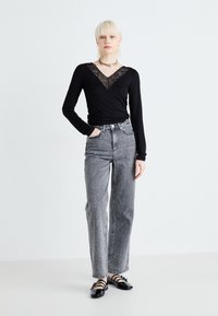 Helanca neagră cu mâneci lungi și decolteu în V din dantelă, asortată cu blugi gri cu talie înaltă, având accente de perle și un design drept.