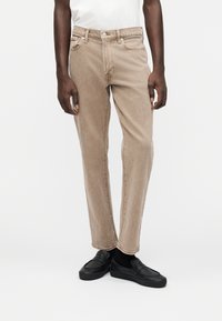 Μπεζ τζιν denim με ίσια γραμμή, πέντε τσέπες και μια διακριτική υφή stone-washed. Συνδυασμένα με μαύρα παπούτσια slip-on.