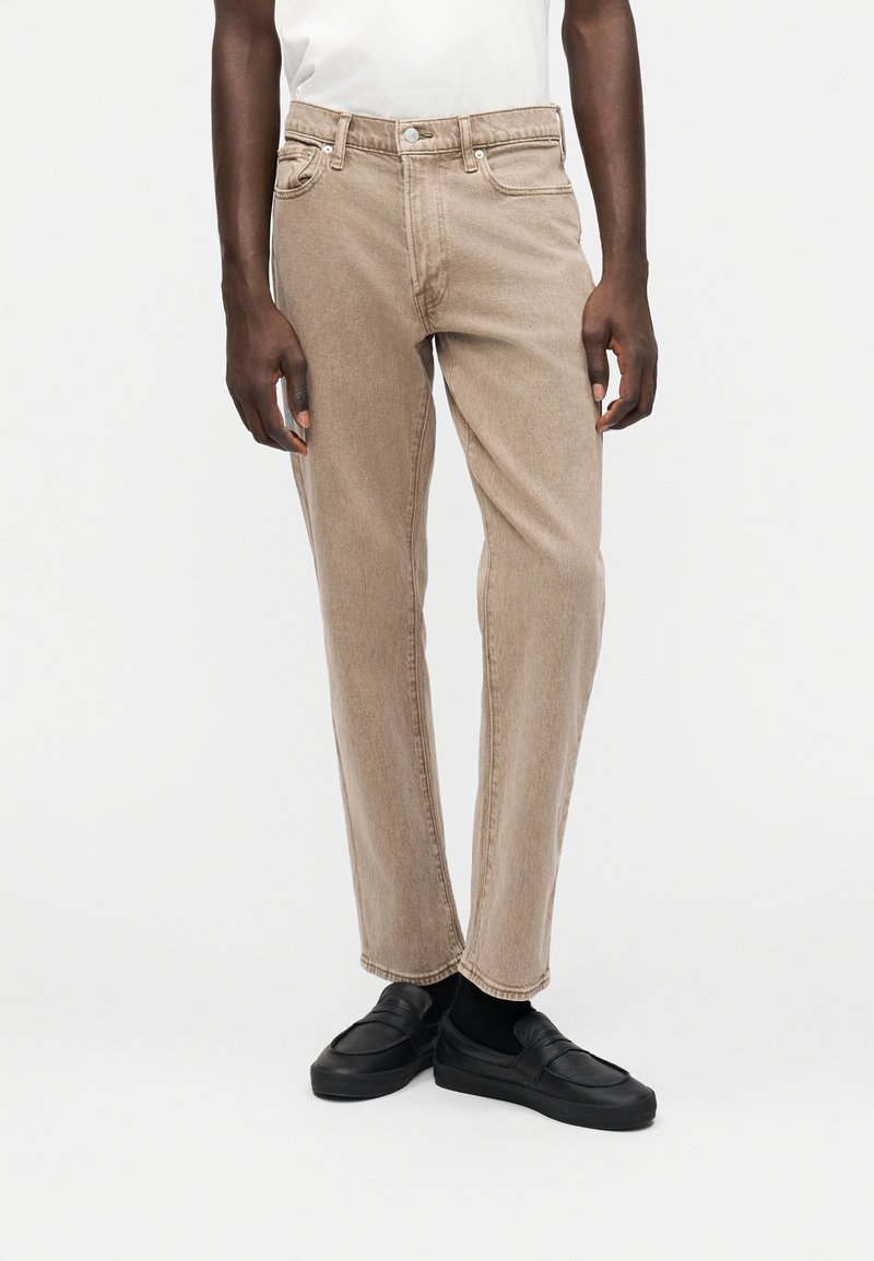 Μπεζ τζιν denim με ίσια γραμμή, πέντε τσέπες και μια διακριτική υφή stone-washed. Συνδυασμένα με μαύρα παπούτσια slip-on.