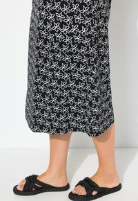 Černá sukně s bílým květinovým vzorem a jemnou texturou. Nosené s černými slip-on sandály se zavázaným popruhem.