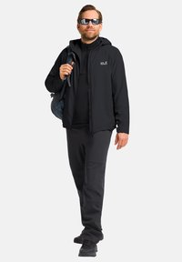 Veste légère noire avec capuche, accompagnée d'un haut à manches longues noir et d'un pantalon. Des lunettes de soleil et un sac bleu complètent le look.