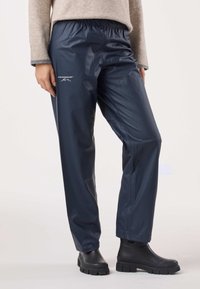 Navy waterproof trousers made of glossy material, featuring an elastic waistband and white logo. Paired with black rubber boots.