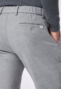 Pantaloni grigi a quadri con vestibilità sartoriale, dotati di tasca laterale e chiusura a bottone sulla tasca posteriore. Texture morbida e design moderno.