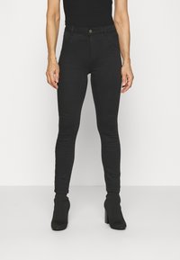 Jeans skinny negros con una cintura de altura media, que presentan bolsillos frontales, costuras mínimas y un diseño elegante, combinados con botas de tacón alto negras.