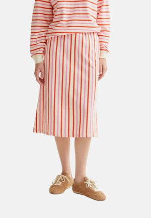 Persona que lleva una falda midi con rayas verticales en rosa, rojo y naranja, una camiseta de manga larga a juego con rayas horizontales y zapatos marrones con cordones.