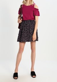 Top fucsia con hombros descubiertos y mangas fruncidas combinado con una falda negra con un patrón de cerezas coloridas. Sandalias negras tipo slide.