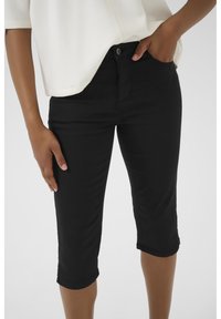 Black knee-length jeans made from stretchy denim, featuring a fitted silhouette, side pockets, and a button closure. Textured fabric finish.
