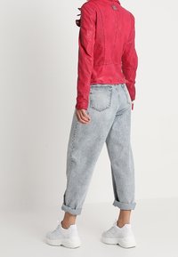 Czerwona skórzana kurtka o fakturowanym wykończeniu, zestawiona z jasnoniebieskimi, luźnymi dżinsami i białymi trampkami na platformie. Zawinięte mankiety dżinsów są widoczne.