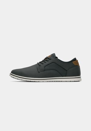 Herren Schnürschuhe aus dunkelgrauem synthetischem Material mit einer weißen Sohle, ausgestattet mit einem braunen Lederakzent an der Ferse und in der Seitenpartie.