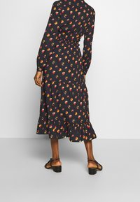 Mustassa kukkakuosisessa mekossa on punaisia ja keltaisia kukkia, pitkät hihat, röyhelöhelma ja istuva vyötärö. Mekko on yhdistetty mustiin korkokenkiin.