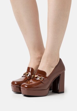 Hnědé lakované platformy s robustním vysokým podpatkem, zdobené zlatým řetízkem a nápodobou perel na přední části.