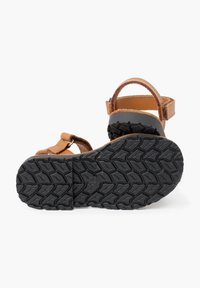 Brązowe skórzane sandały z regulowanym paskiem, wytrzymała czarna gumowa podeszwa oraz teksturowany wzór bieżnika zapewniający przyczepność. Odkryta konstrukcja wkładki.