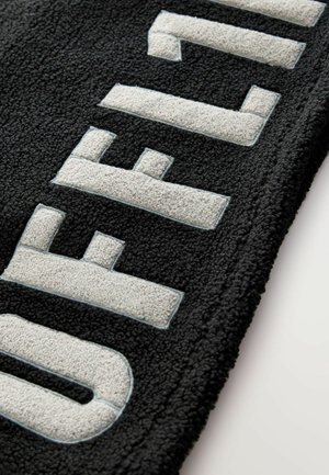 Černý fleecovýkoberec s vyvýšeným šedým textem, který říká "OFFLINE", s texturovaným povrchem a kontrastním modrým obrysem kolem písmen.