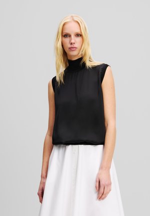 Haut sans manches noir avec un col montant, présentant une texture lisse et une coupe décontractée, associé à une jupe blanche à boutons.