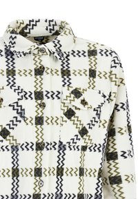 Chaqueta de camisa de felpa blanca con patrón de cuadro zigzagueante en negro y verde oliva, cierre frontal de botones, dos bolsillos en el pecho con botones y cuello.