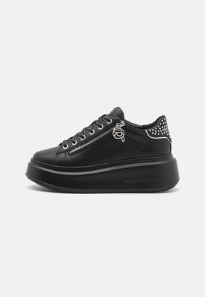 Black platform sneakers with a smooth leather upper, silver eyelets, side zipper, and studded accents on the heel. Branding on the sole.