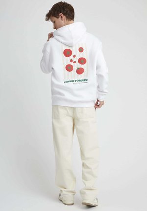 Hoodie blanc avec un graphique de tomate coloré dans le dos, comprenant des tomates rouges et des étoiles vertes sur un fond rayé beige.