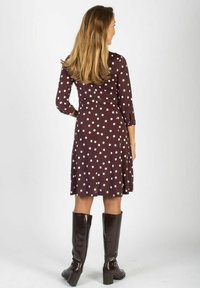 Brązowa sukienka w grochy z rękawami do łokcia, rozkloszowanym dołem i teksturowaną tkaniną, zestawiona z wysokimi brązowymi kozakami.