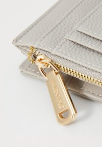 Portafoglio in pelle grigia con texture, dotato di cerniera e hardware dorati, presenta una forma rettangolare e dettagli cuciti sulla superficie.