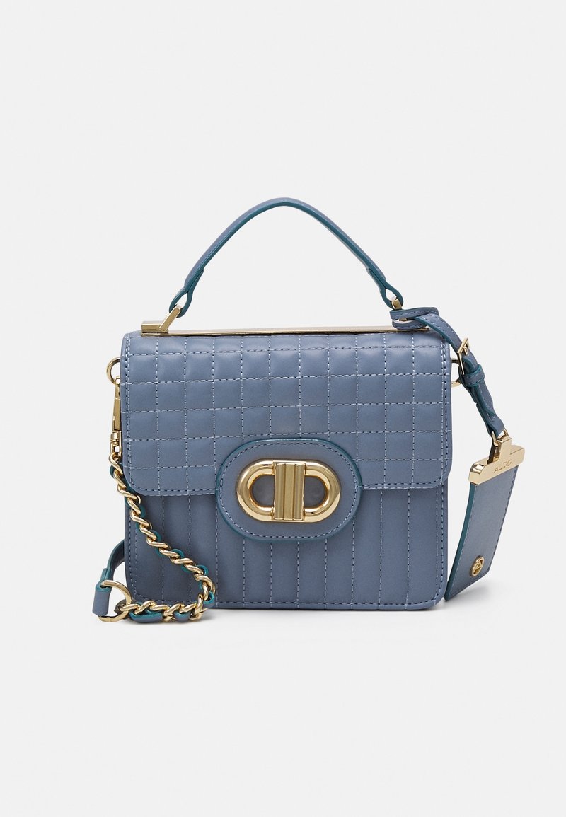 Sac à main matelassé bleu avec bandoulière en chaîne dorée, poignée supérieure et fermoir ovale doré sur fond plat clair.