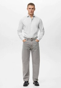 Witte langemouwen blouse, grijze rechte jeans en zwarte schoenen. Focus op de textuur van de stof en strakke lijnen. Geen zichtbare patronen of logo's.