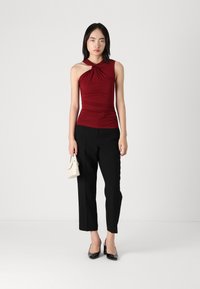 Top sin mangas burdeos con escote torcido, acompañado de pantalones negros a medida y zapatos de tacón negros. Bolso blanco como accesorio.