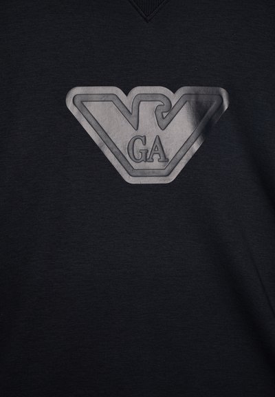 Μαύρη μπλούζα με κοντά μανίκια που διαθέτει τρισδιάστατο, ασημένιο λογότυπο με τα γράμματα "GA" μέσα σε γεωμετρικό σχέδιο, κατασκευασμένη από μαλακό βαμβακερό ύφασμα.