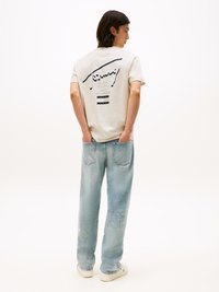 T-shirt de mangas curtas creme com impressão gráfica nas costas, combinado com jeans de corte solto azul claro e ténis brancos. Textura suave em todo o tecido.