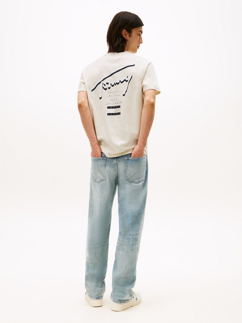 T-shirt de mangas curtas creme com impressão gráfica nas costas, combinado com jeans de corte solto azul claro e ténis brancos. Textura suave em todo o tecido.