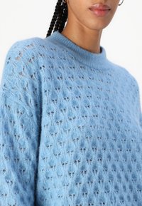 Hellblauer Strickpullover mit strukturiertem Offenmuster, Rundhalsausschnitt und langen Ärmeln. Hergestellt aus weichem, leichtem Material.