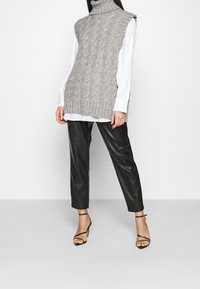 Jersey de punto sin mangas en gris claro con un patrón de trenzas, combinado con pantalones de cuero sintético negros y tacones negros con tiras.