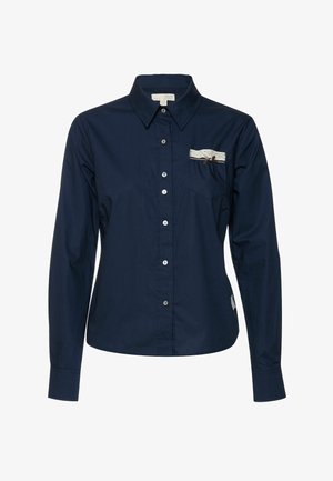 Laivastonsininen pitkähihainen nappikauluspaita, jossa on kaulus, yksittäinen rintatasku, jossa pitsireunus ja koristeellinen rusetti. Sileä pinta.