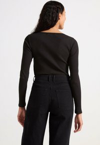 Maglietta nera a costine con maniche lunghe abbinata a jeans scuri a vita alta, caratterizzata da una silhouette aderente e da dettagli in cucitura discreti sulla schiena.