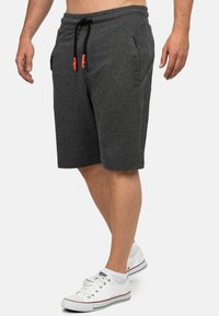 Grijze katoenmix shorts met een elastische tailleband en zwart trekkoord. Voorzien van twee zijzakken en een knielange snit. Draagt met witte sneakers.
