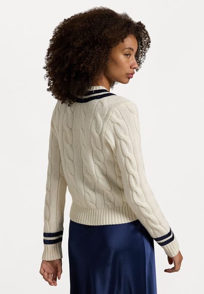 Pull en maille torsadée crème avec des accents de rayures navy au col et aux poignets. Ourlet et manches côtelés créent une silhouette ajustée.