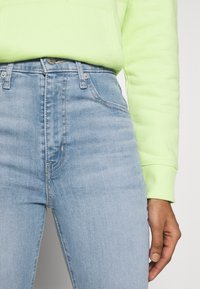 Jeans de cintura alta en un azul claro de denim con una textura suave, que cuentan con cinco bolsillos, cierre de cremallera y costuras decorativas.