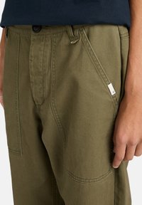 Khaki broek van katoen, met een rechte snit, zijzakken en een zichtbare knoopsluiting. De stof is glad en duurzaam.