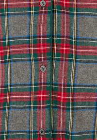 Gros plan sur un tissu à carreaux boutonné présentant des rayures horizontales et verticales rouges, vertes, grises, bleues, jaunes, noires et blanches.