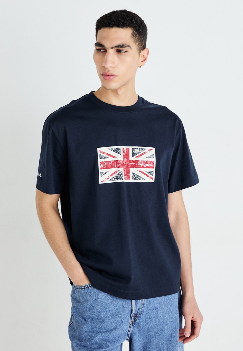 Tumši zils kokvilnas T-krekls ar nolietotu Union Jack grafiku uz priekšpuses. Īsas piedurknes un brīva piegriezuma ar apaļu kakla izgriezumu.