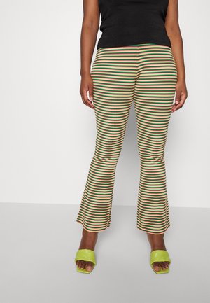 Calças largas listradas em amarelo, vermelho e verde com uma textura nervurada. Combinadas com sandálias rasteiras trançadas verdes. Top preto não descrito.